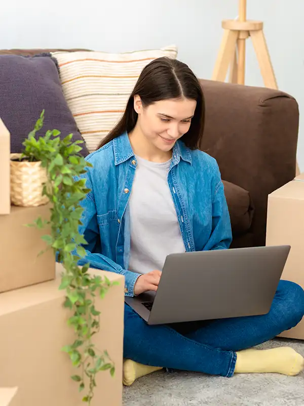 woman working on laptop sitting on floor with moving boxes