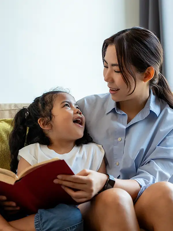 mother and daughter reading book on couch